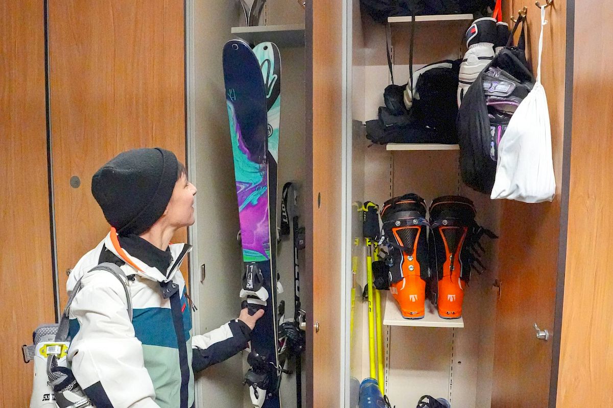 A person is organizing ski gear in a locker that includes skis, ski poles, boots, helmets, gloves, and other skiing accessories.
