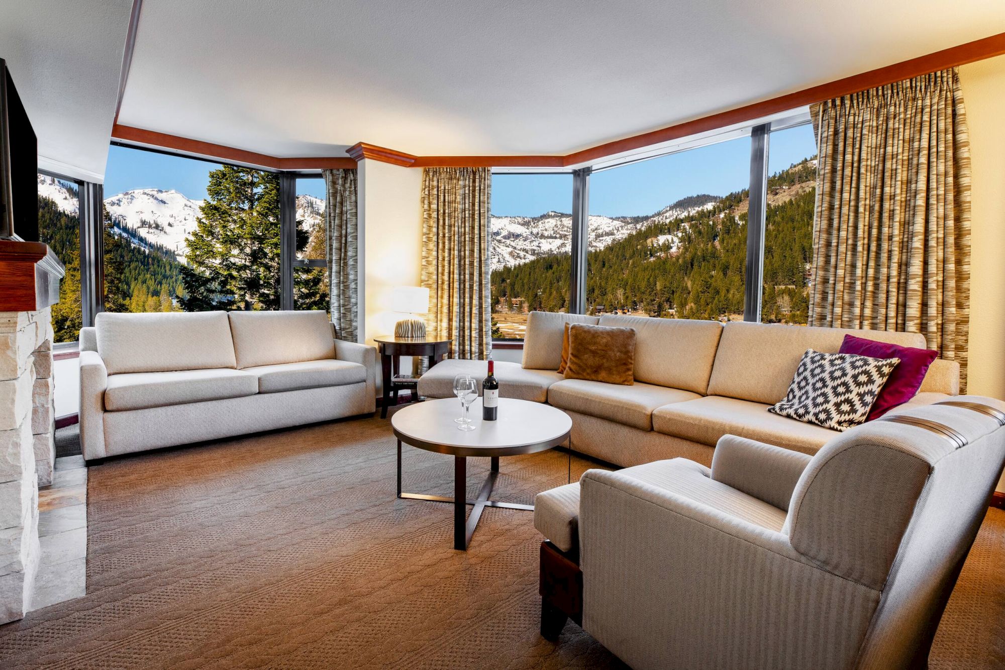 A cozy living room with large windows, three couches, a table, and a scenic mountain view.