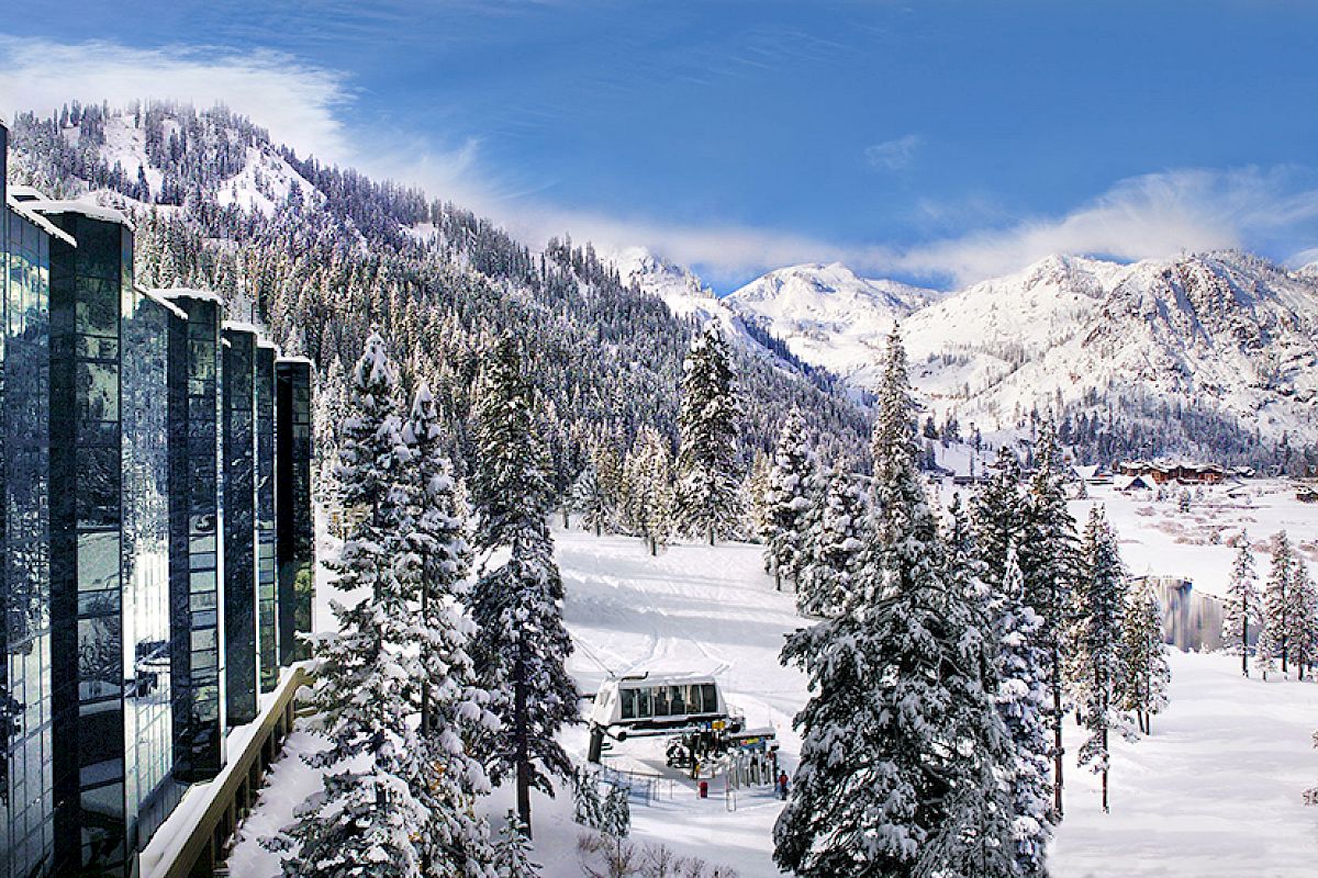 A snowy mountain landscape with a modern building on the left, surrounded by pine trees and a ski lift in the center of the image.